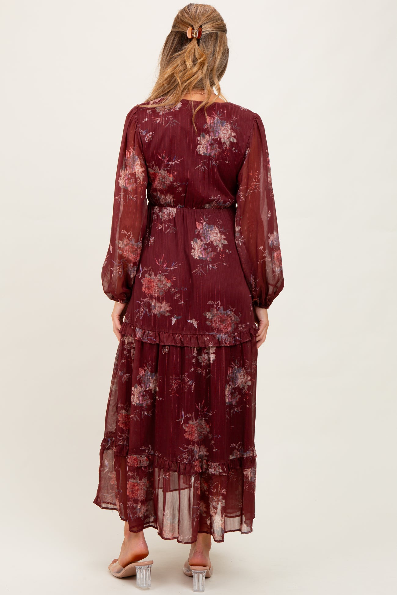 woman wearing a burgundy floral maternity maxi dress with long sleeves and a tiered skirt, showing a baby bump