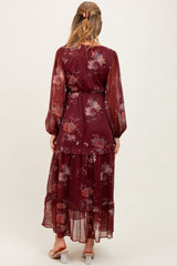 woman wearing a burgundy floral maternity maxi dress with long sleeves and a tiered skirt, showing a baby bump