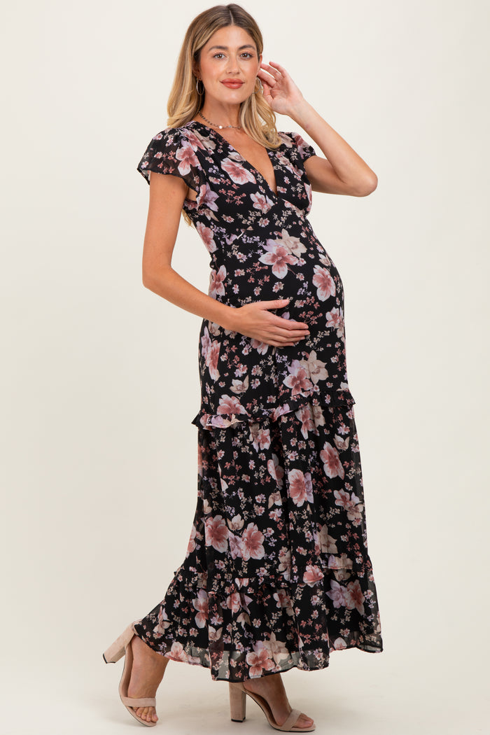 woman wearing a black floral maternity maxi dress, showing baby bump and standing with one hand on her belly