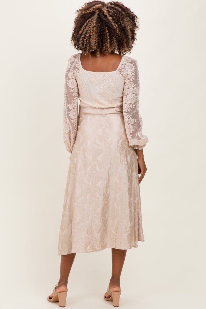 woman wearing a light beige maternity dress with sheer long sleeves and a flowy skirt, showing the back view