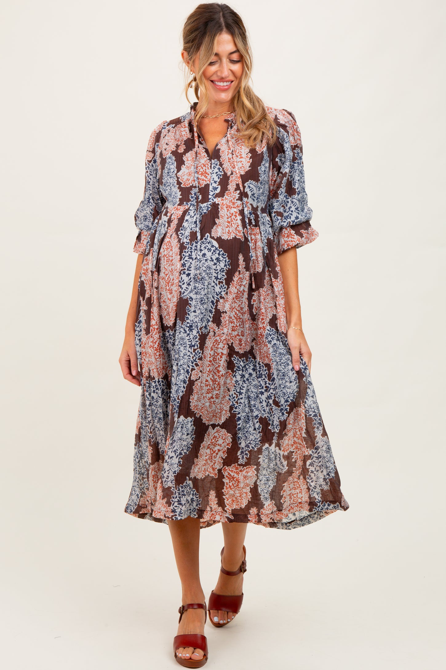 woman wearing a multicolored floral print maternity dress with three-quarter sleeves and a baby bump visible