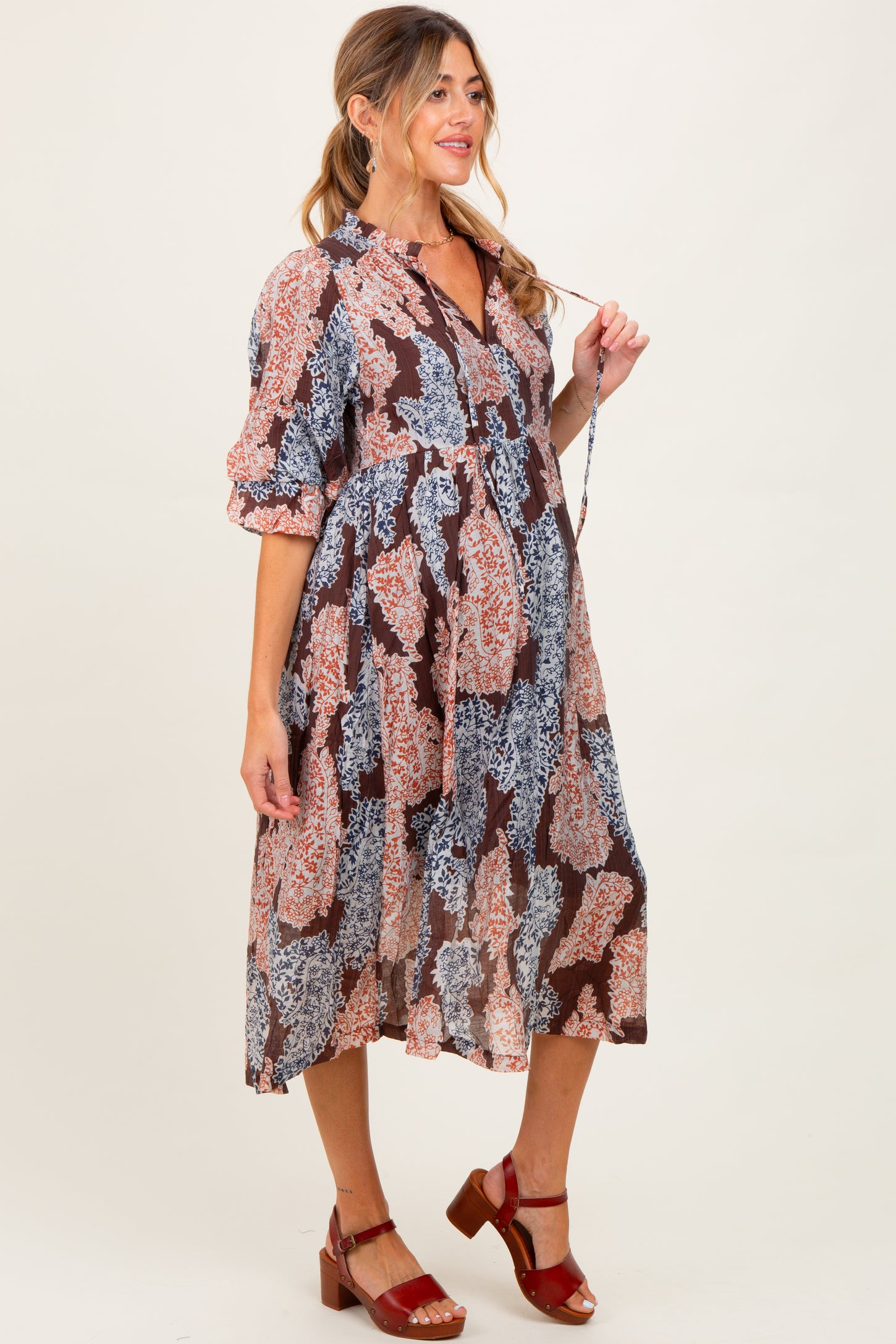 woman wearing a floral print maternity dress with short sleeves and a flowing skirt, holding her baby bump