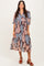 woman wearing a brown floral midi dress with bell sleeves and a loose fit, standing and smiling
