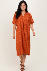 woman wearing an rust orange midi dress with puff sleeves and a relaxed fit, standing against a neutral background