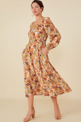 woman wearing a floral midi dress with long sleeves and pockets, styled with tan heeled sandals