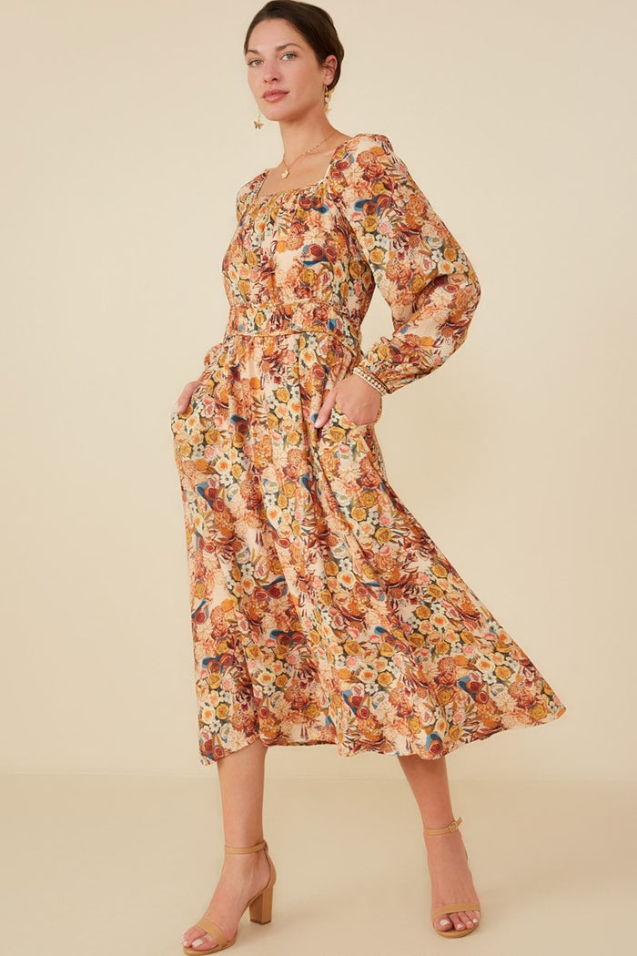 woman wearing a floral midi dress with long sleeves and pockets, styled with tan heeled sandals