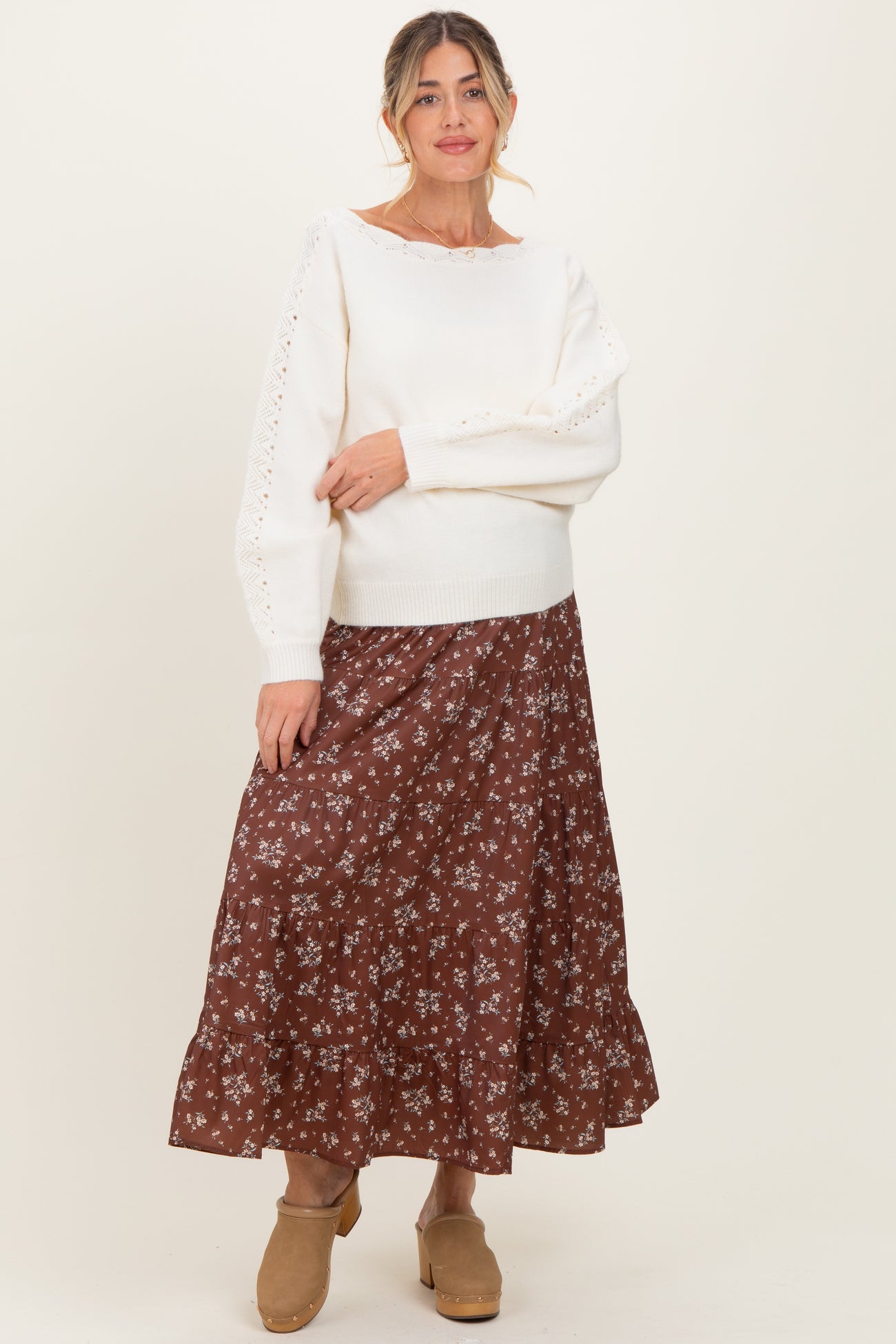 woman wearing a cream maternity sweater with lace details and a brown floral maternity skirt, smiling at the camera