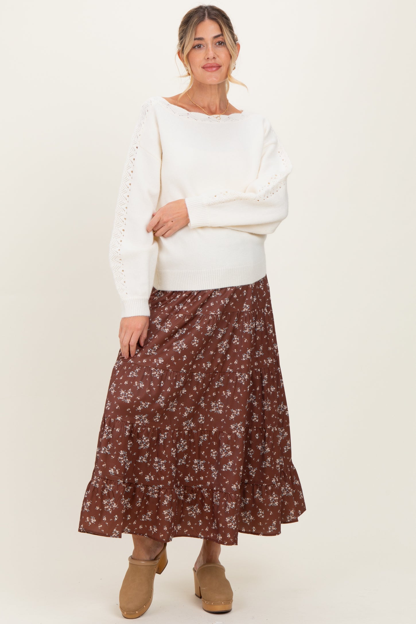 woman wearing a cream maternity sweater with lace details and a brown floral maternity skirt, smiling at the camera