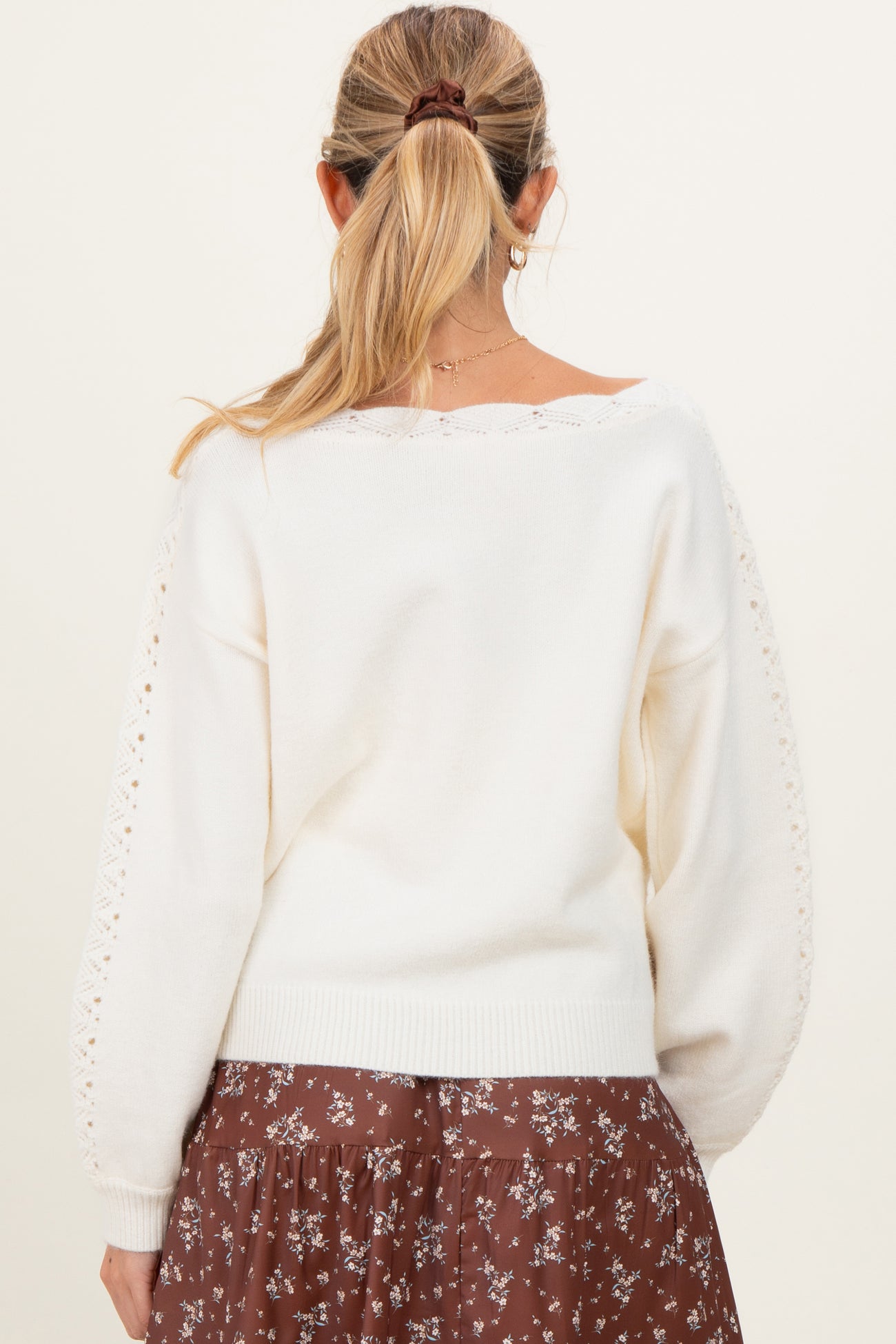 woman wearing a white maternity sweater with lace detailing on the sleeves, seen from the back