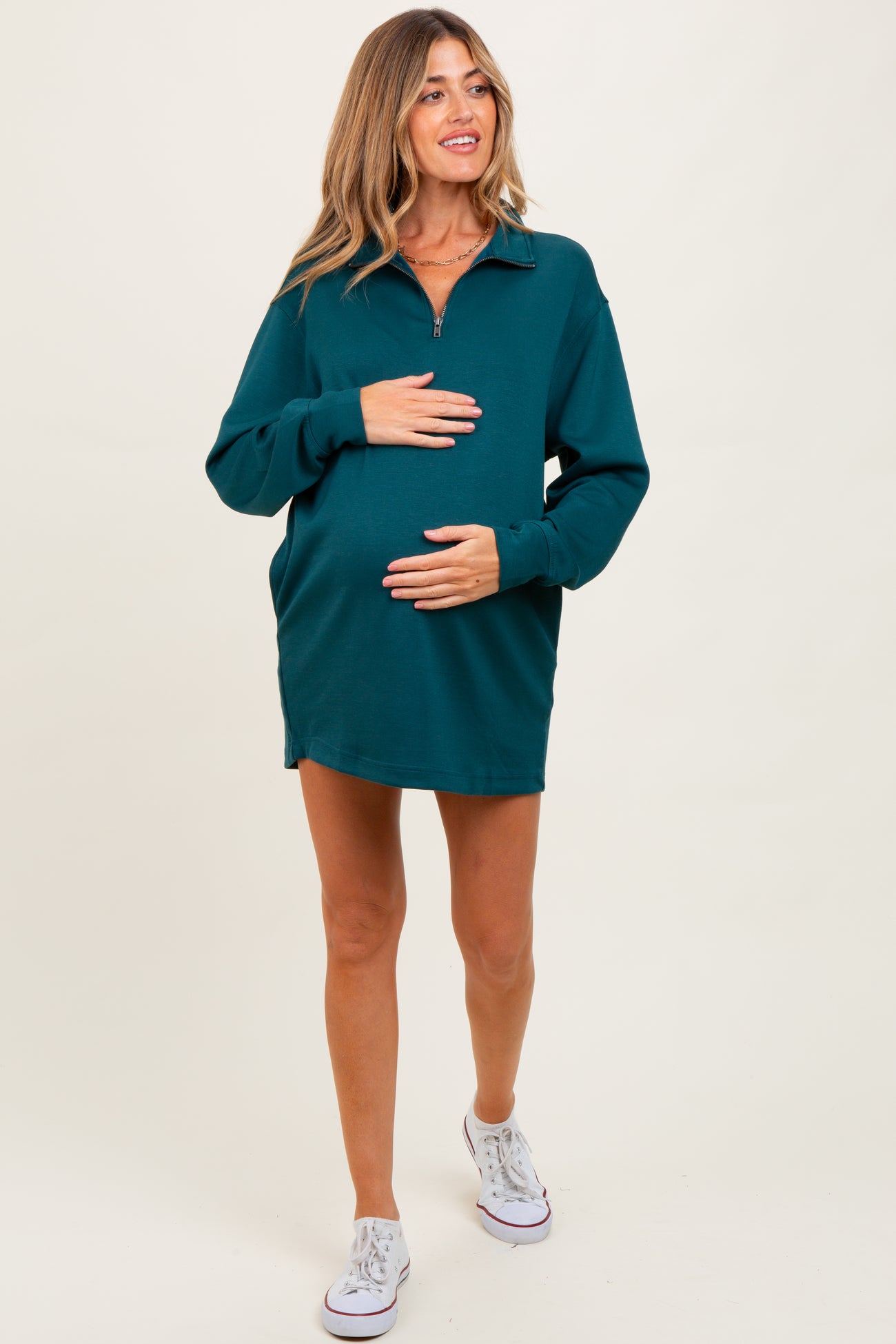 woman wearing a teal long sleeve maternity dress with a zip collar and holding her baby bump