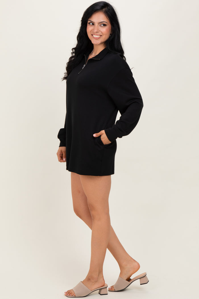woman wearing a black oversized zip-up dress with long sleeves and pockets, standing on a neutral background