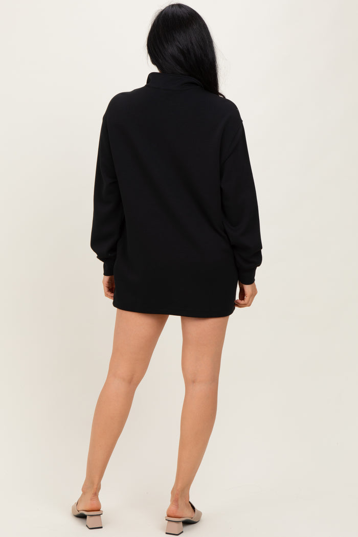 woman wearing a black oversized pullover dress with long sleeves and a high collar, shown from the back