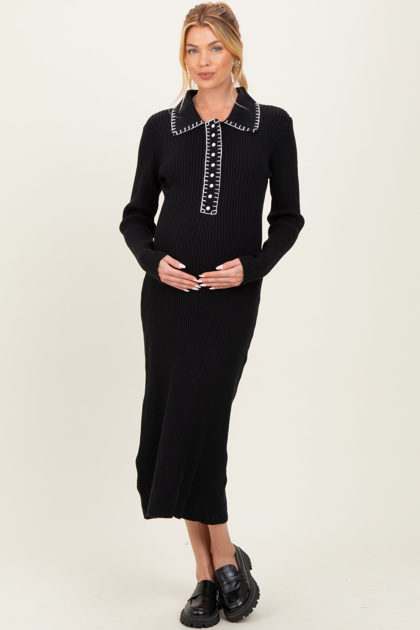woman wearing a black ribbed maternity dress with a collar and button details, holding her baby bump