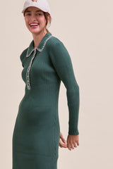 woman wearing a ribbed green dress with a collared neckline and long sleeves, smiling against a neutral background