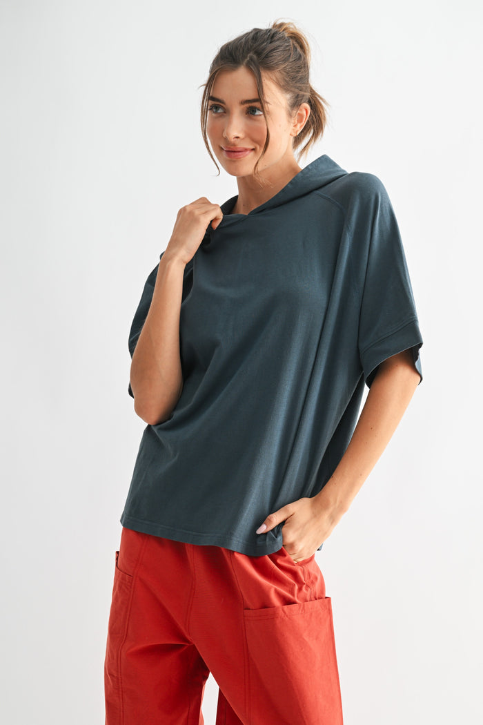 woman wearing a dark teal oversized hoodie with short sleeves and relaxed fit, paired with red wide-leg pants