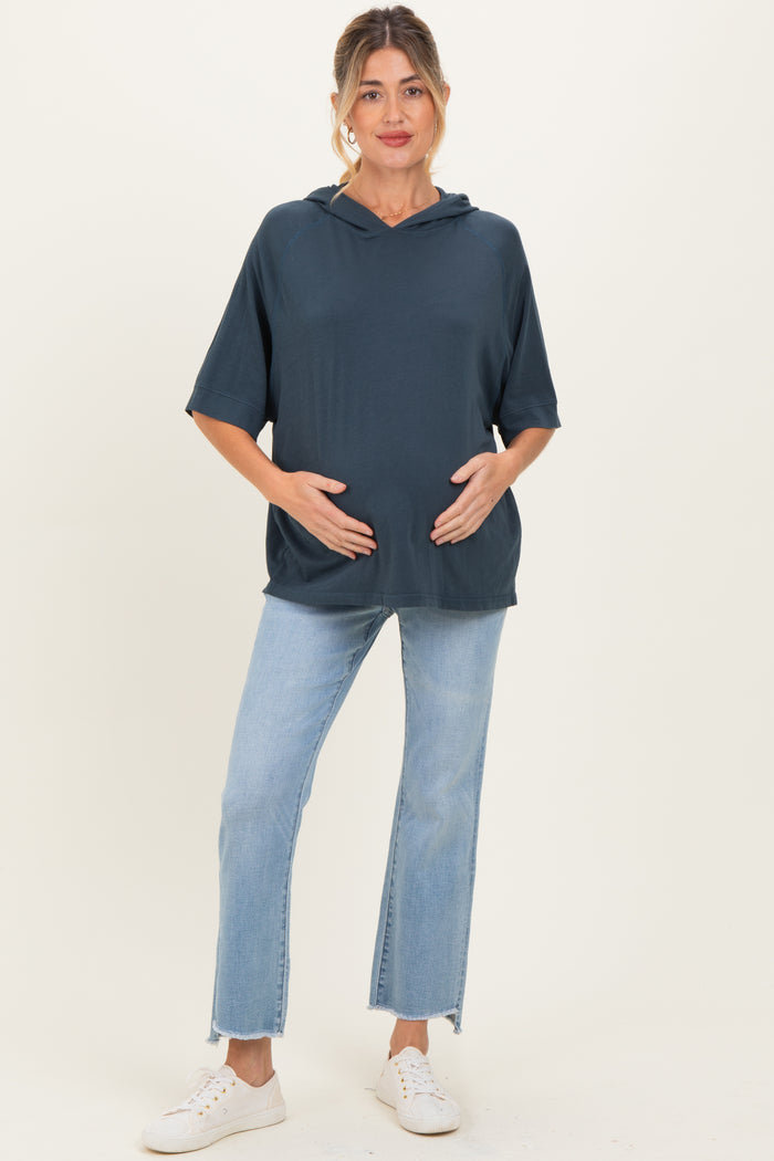 woman wearing a dark blue short sleeve maternity hoodie and holding her baby bump with light wash jeans