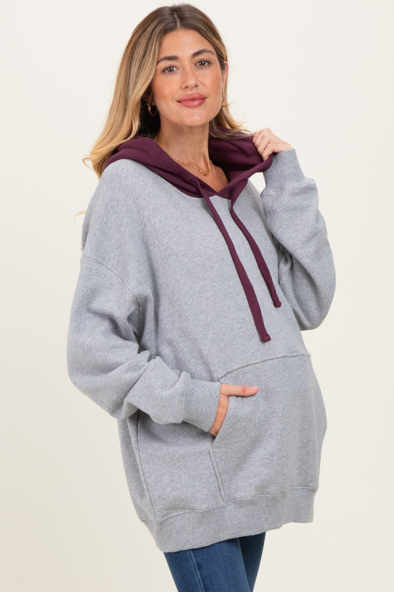 woman wearing a gray oversized maternity hoodie with a maroon hood and pocket, looking at the camera with a smile