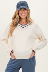 woman wearing a cream maternity sweater with a navy striped v-neck and holding her baby bump