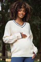 woman wearing a cream maternity sweater with navy blue accents and holding her baby bump
