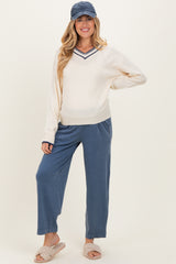 woman wearing a cream maternity sweater with a v-neck and navy stripes, paired with blue maternity jogger pants