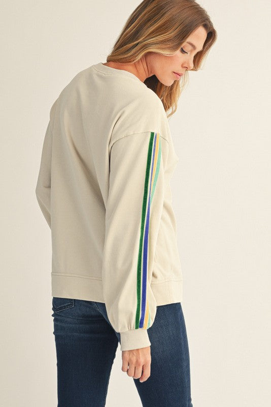 woman wearing a beige sweatshirt with colorful striped sleeves and denim jeans, facing away from the camera