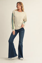 woman wearing a cream long sleeve sweatshirt with multicolored stripe details and flared denim jeans