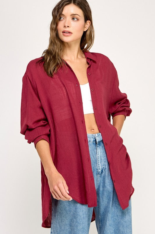 woman wearing a long burgundy button-up shirt over a white crop top and high-waisted blue jeans