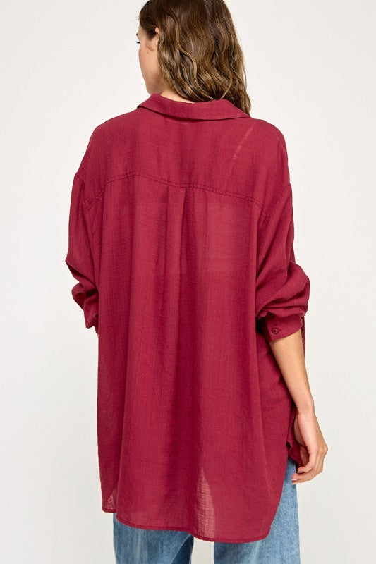 woman wearing a loose-fitting burgundy button-up shirt with rolled sleeves and a relaxed back design