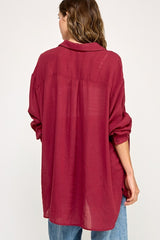 woman wearing a loose-fitting burgundy button-up shirt with rolled sleeves and a relaxed back design