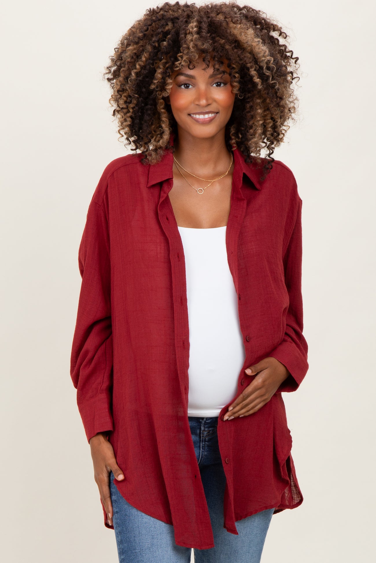 woman wearing a burgundy maternity button-up shirt and showing her baby bump with a confident smile