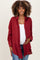 woman wearing a burgundy maternity button-up shirt and showing her baby bump with a confident smile