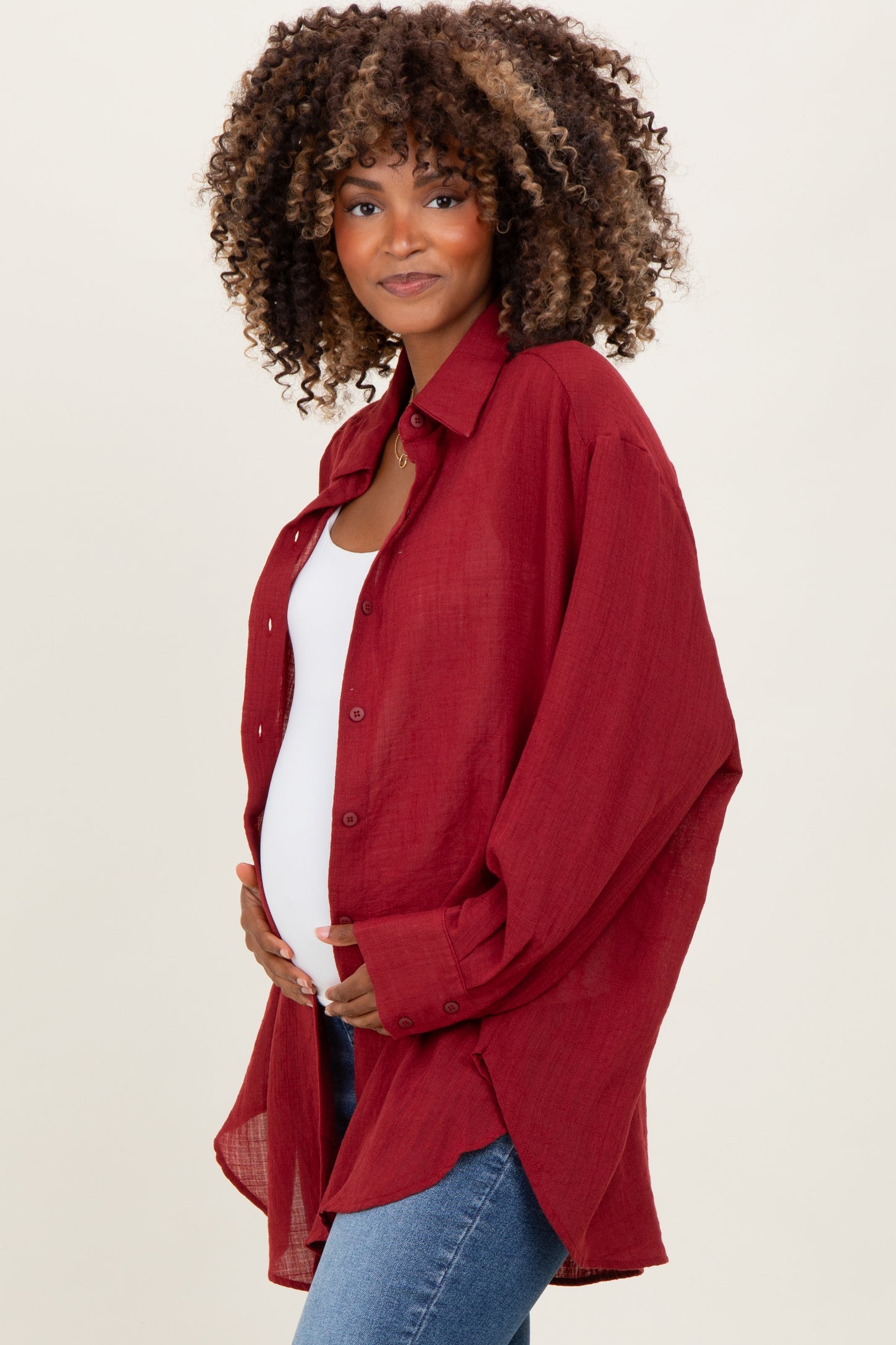 woman wearing a burgundy oversized maternity button-up shirt and holding her baby bump