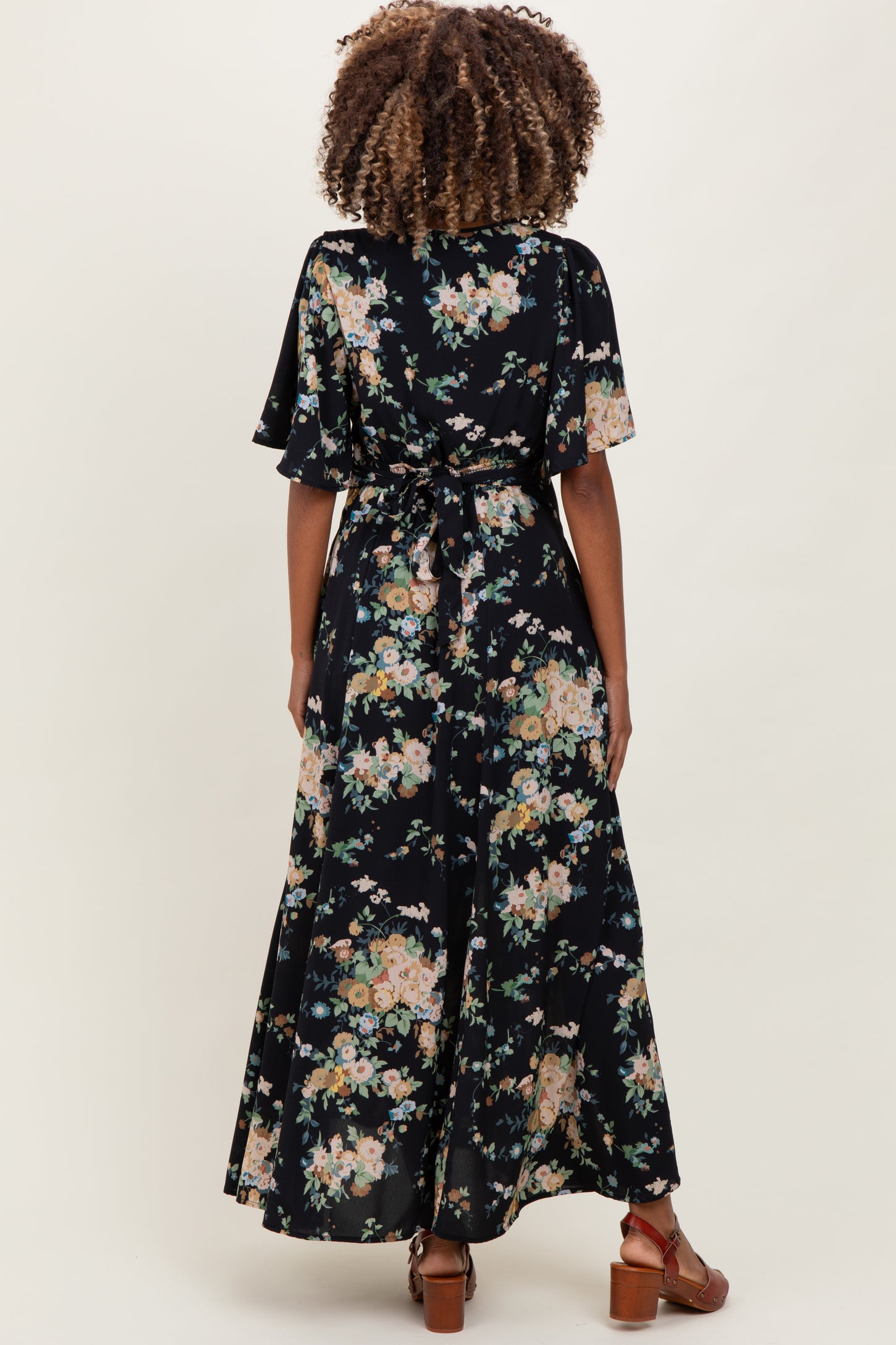 woman wearing a black floral maternity maxi dress with flutter sleeves and a tied waist, showing a baby bump from the back