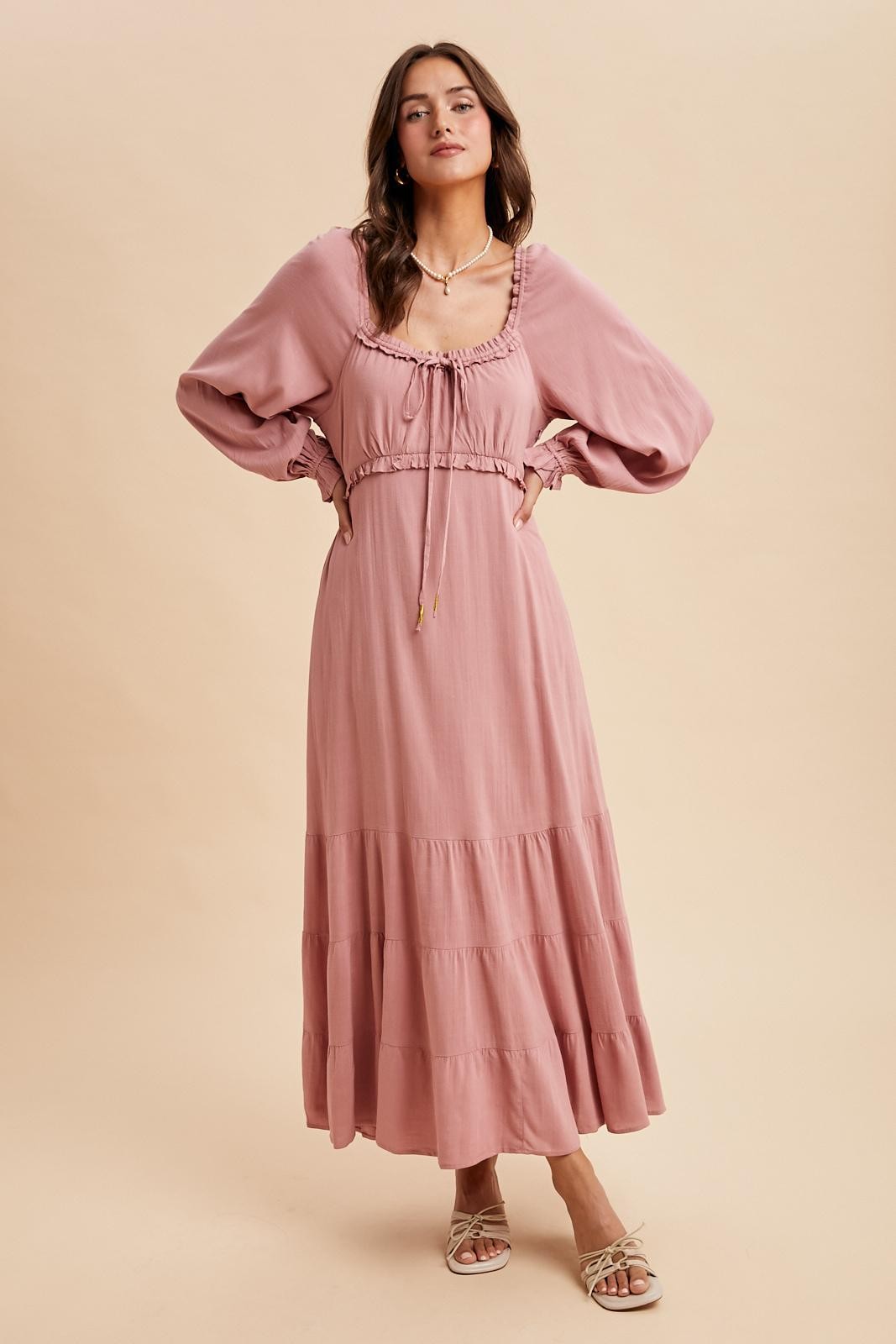 woman wearing a dusty pink long sleeve maxi dress with a tiered skirt and drawstring detail around the neckline