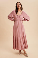 woman wearing a dusty pink long sleeve maxi dress with a tiered skirt and drawstring detail around the neckline
