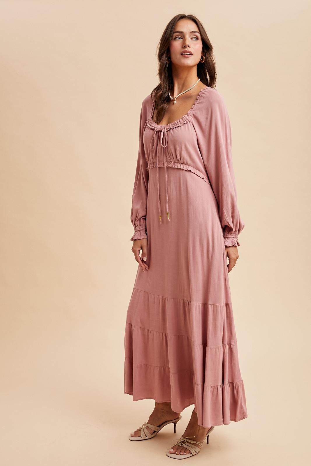 woman wearing a dusty rose long sleeve maxi dress with a drawstring neckline and tiered skirt