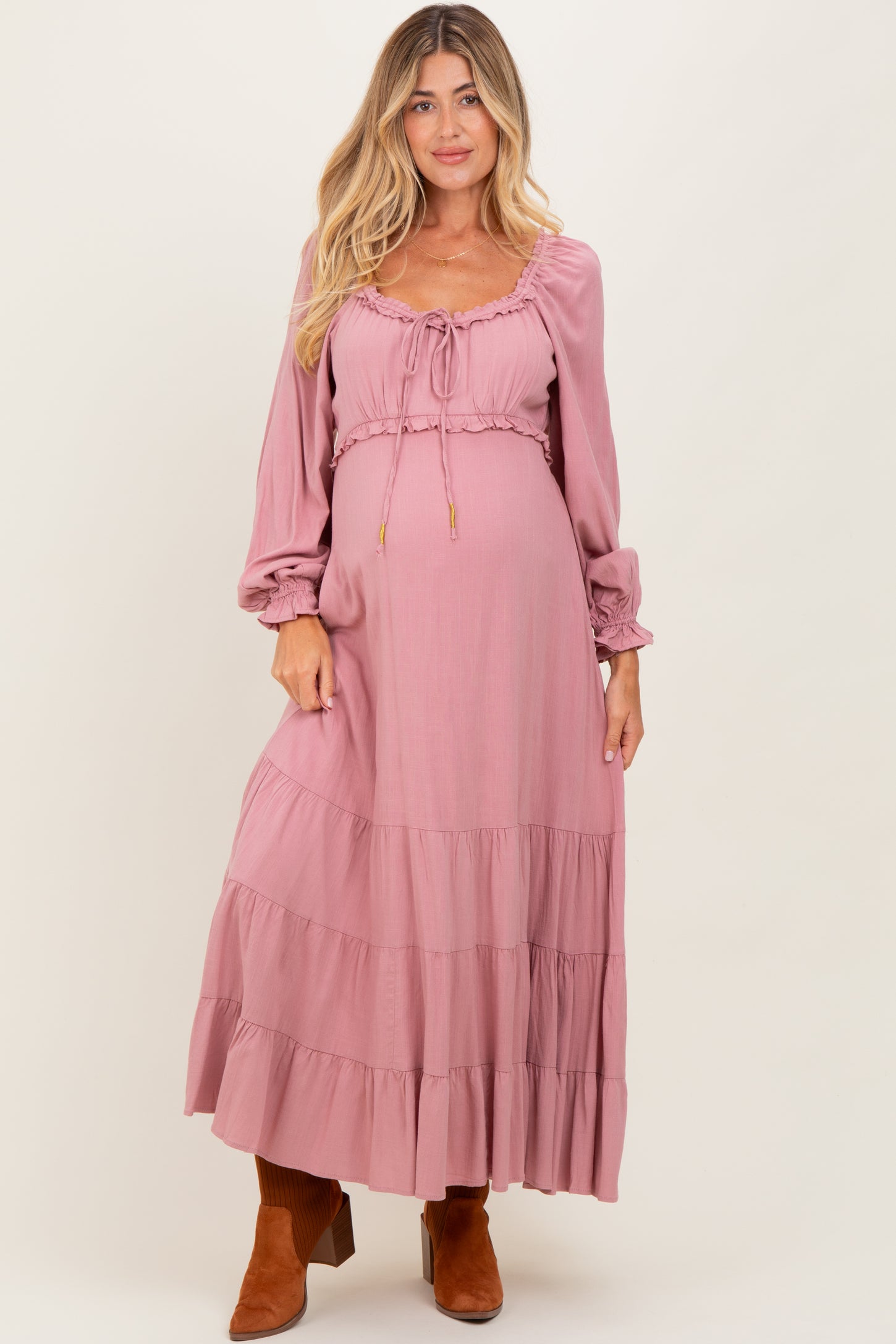woman wearing a dusty pink maternity maxi dress with long sleeves and tiered ruffles, showing a baby bump