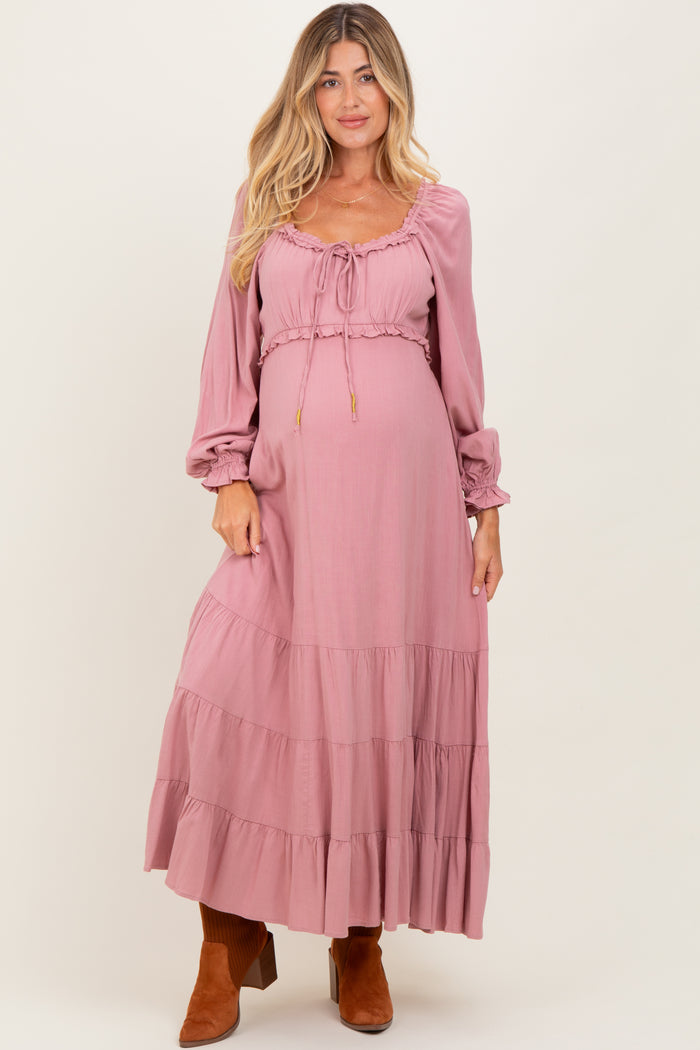 woman wearing a dusty pink maternity maxi dress with long sleeves and tiered ruffles, showing a baby bump