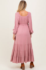 woman wearing a dusty pink maternity maxi dress with long sleeves and tiered skirt, showing a baby bump from behind