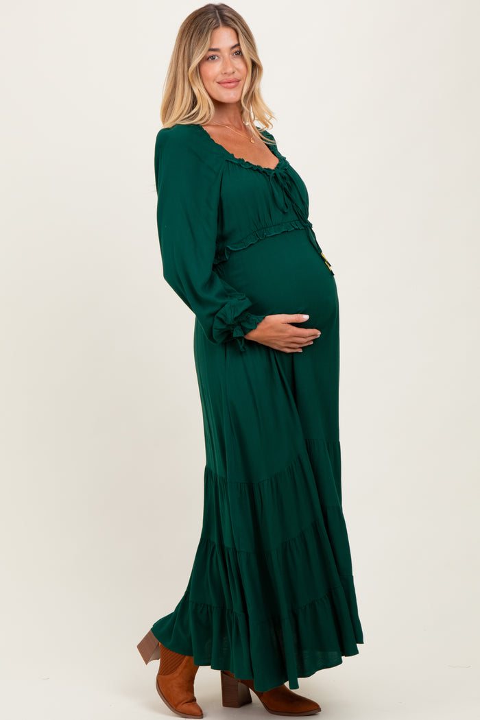 woman wearing a green long sleeve maternity dress with ruffle details and holding her baby bump