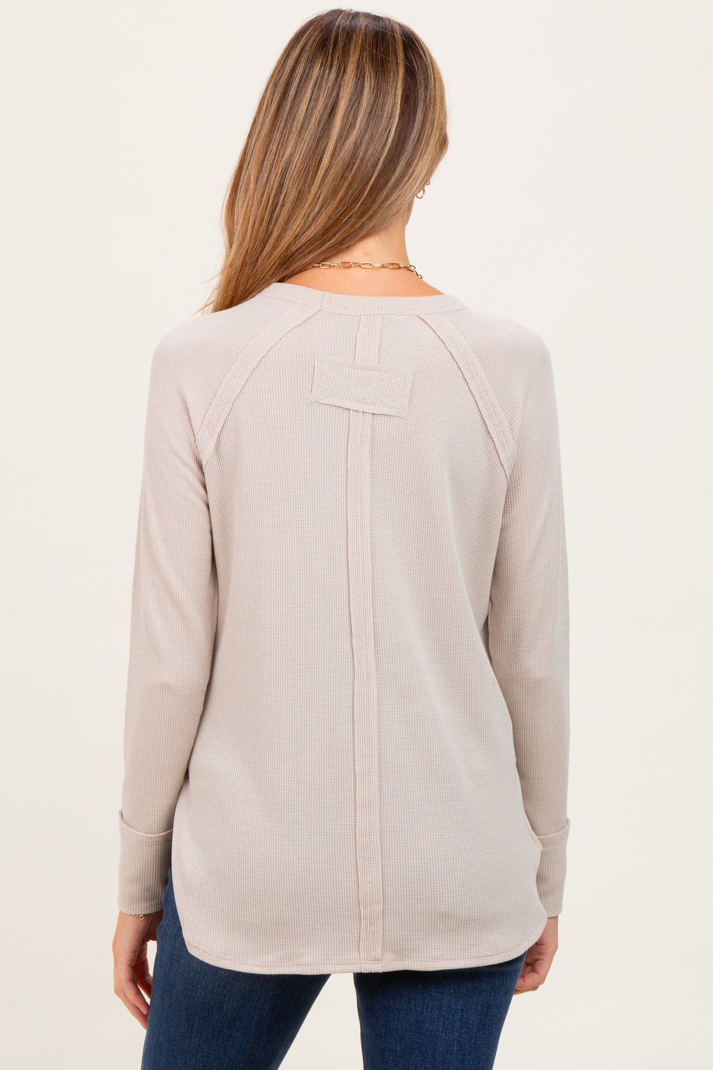 woman wearing a beige long sleeve maternity top with a back detail and relaxed fit