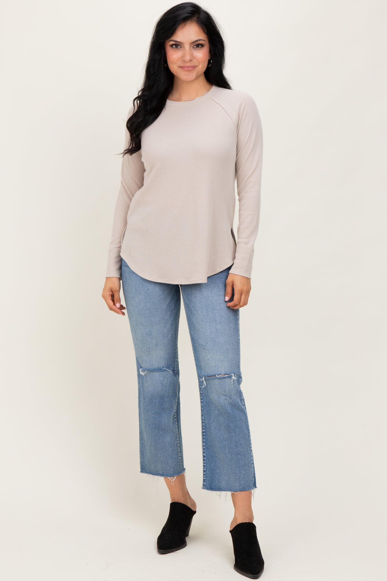 woman wearing a beige long sleeve ribbed top with a curved hem and light blue frayed hem jeans