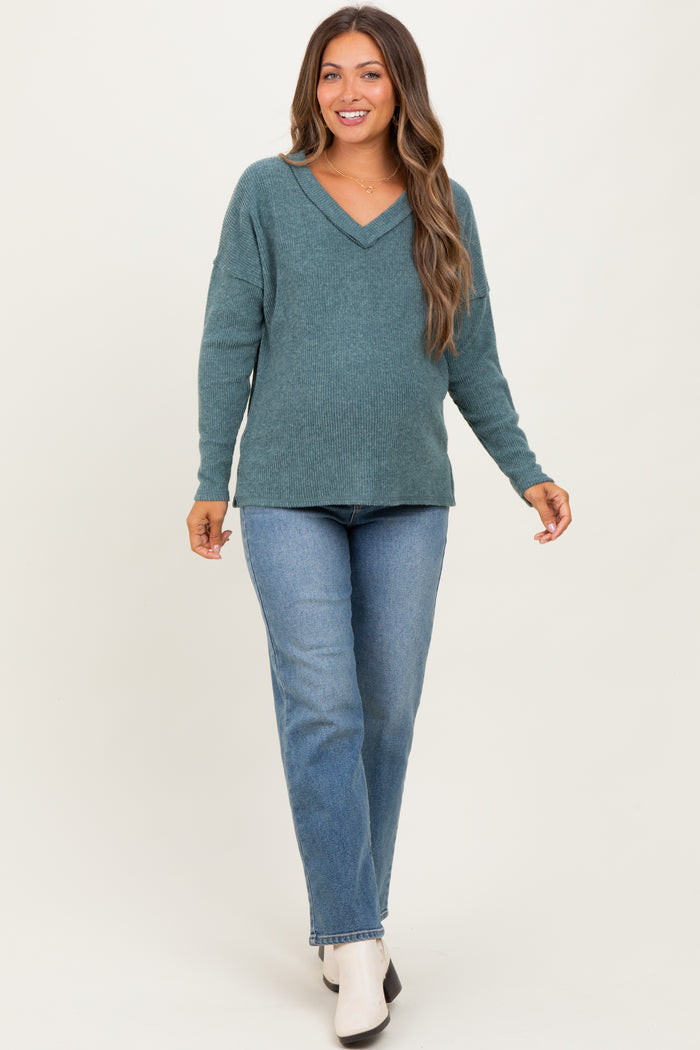 woman wearing a teal v-neck maternity sweater and blue jeans, with a visible baby bump
