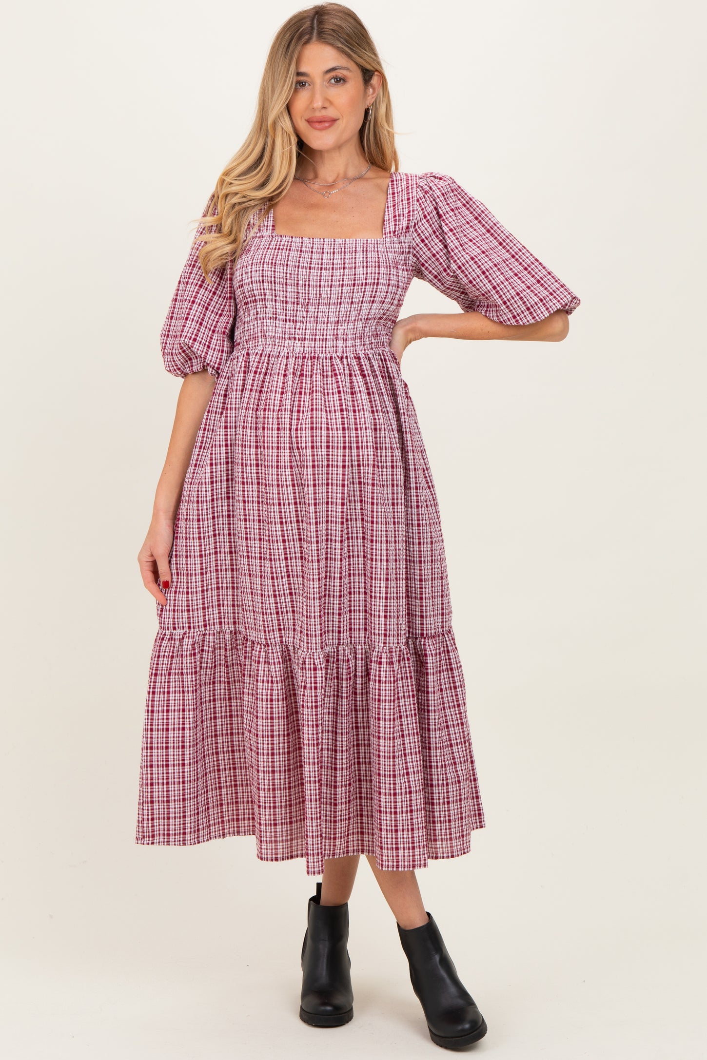 woman wearing a pink and white checkered maternity dress with puff sleeves and a tiered skirt, showing a baby bump