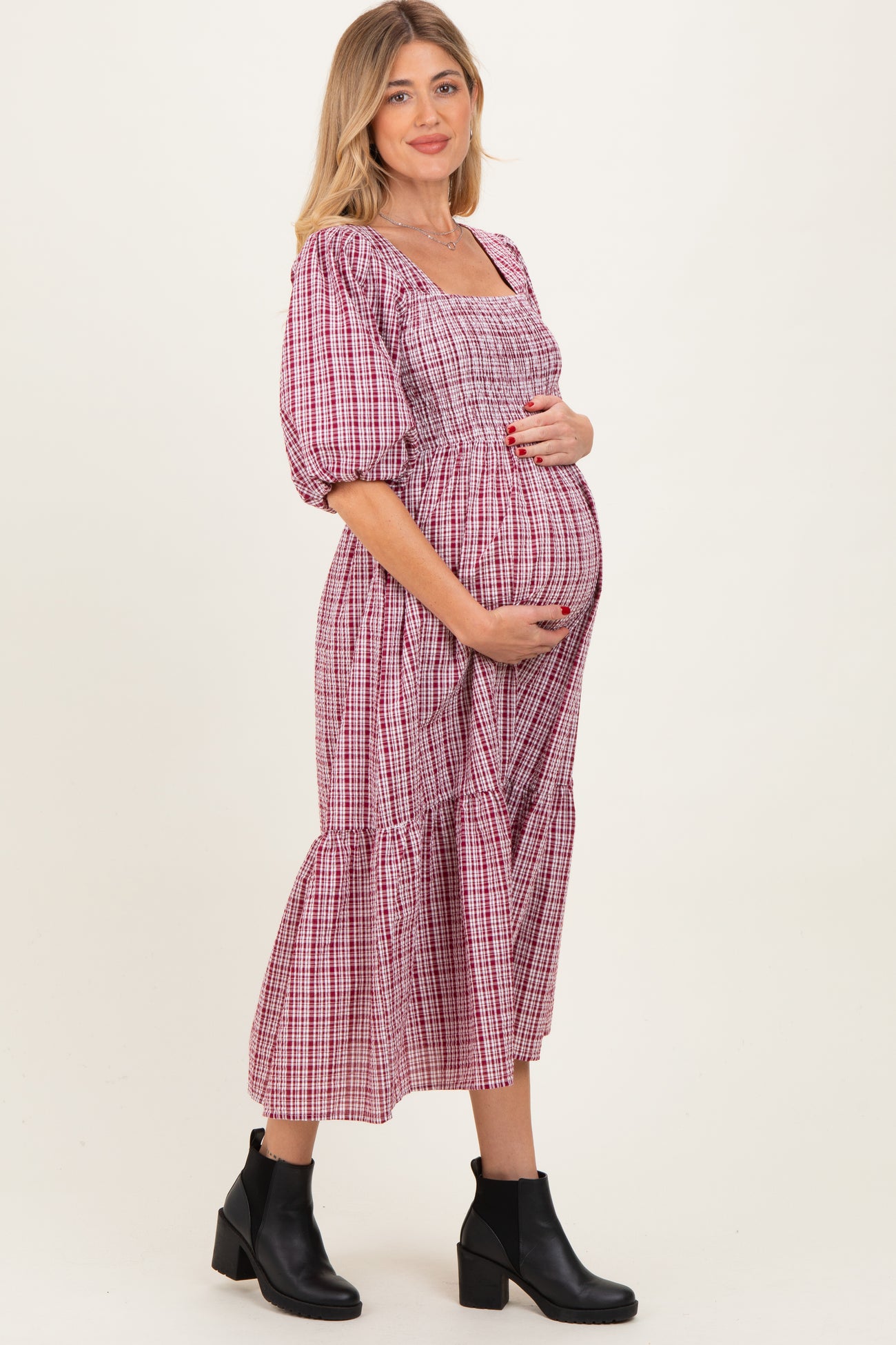 woman wearing a pink and white checkered maternity dress with puff sleeves and a tiered skirt, holding her baby bump