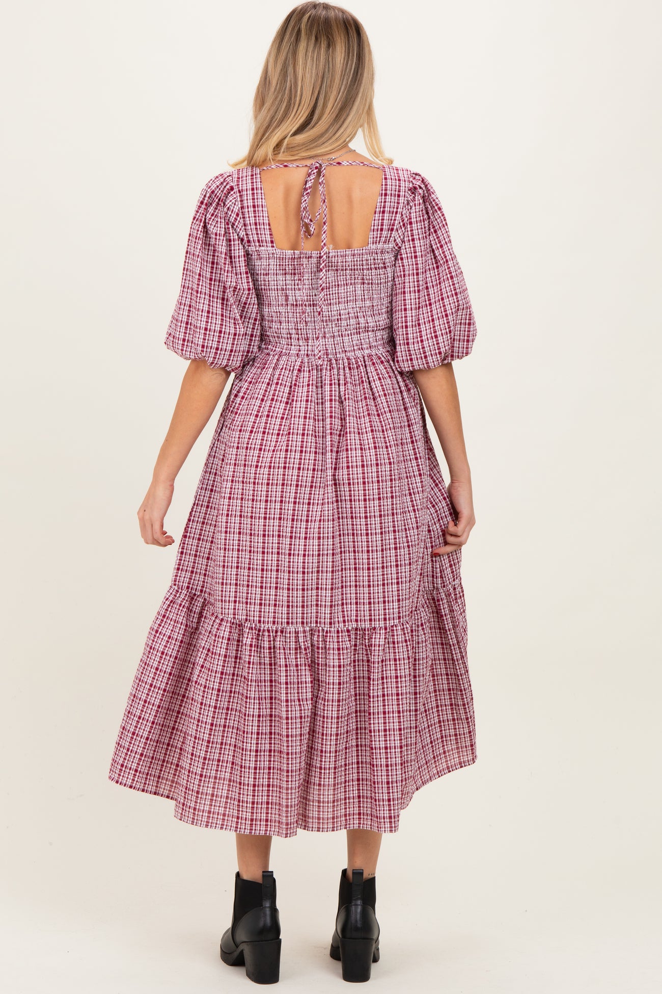 woman wearing a red and white checkered maternity dress with puff sleeves and a tiered hem, showing the back view