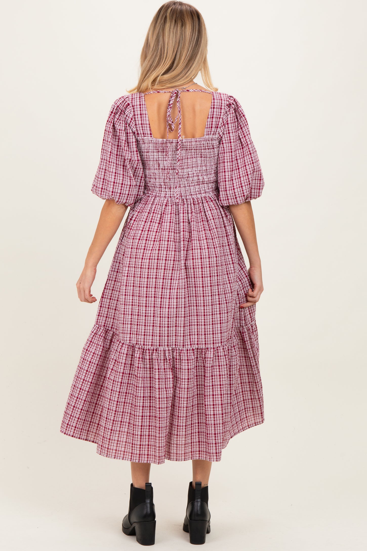 woman wearing a red and white checkered maternity dress with puff sleeves and a tiered hem, showing the back view