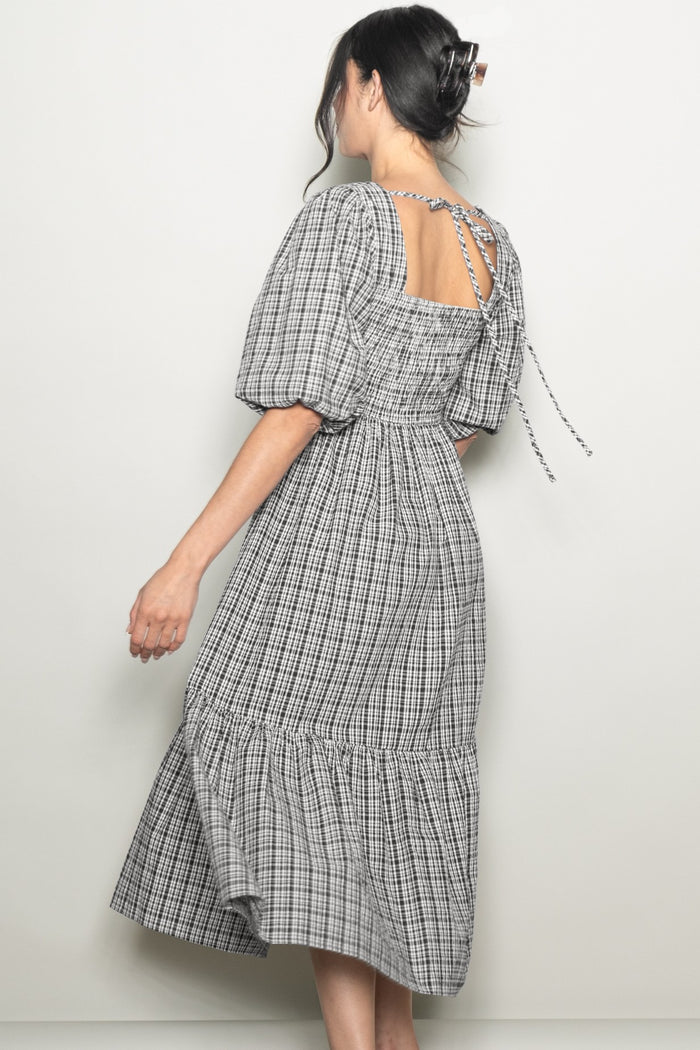 woman wearing a black and white gingham midi dress with puff sleeves and a tied open back detail