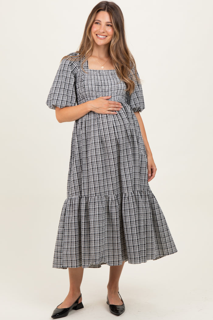 woman wearing a black and white checkered maternity dress with puff sleeves and a tiered hem, holding her baby bump
