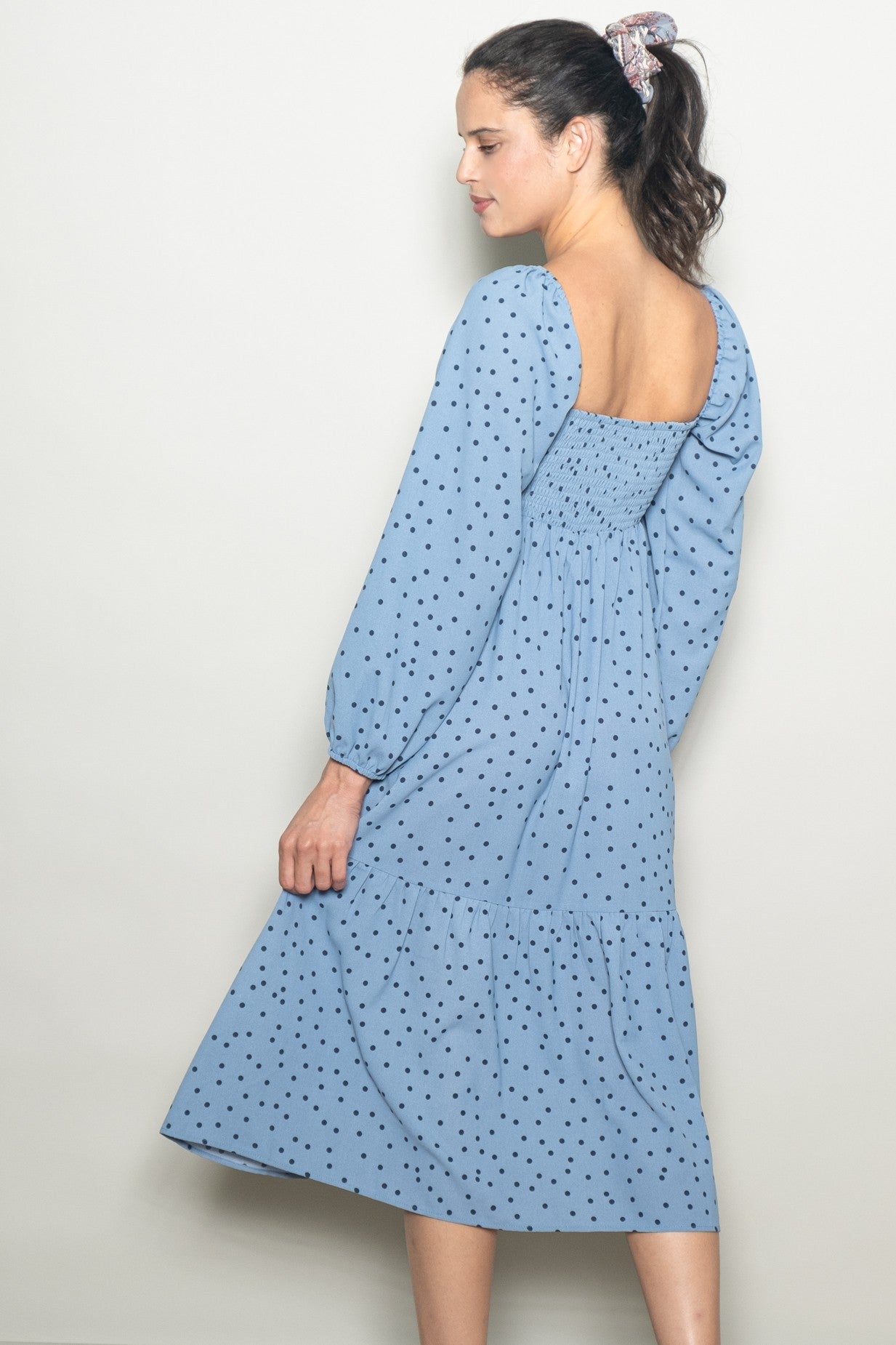 woman wearing a light blue midi dress with black polka dots and puff sleeves, shown from the back